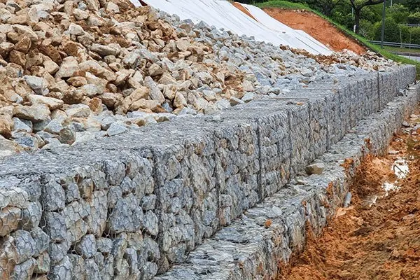 Wire gabion baskets filled with rock retaining a cut embankment